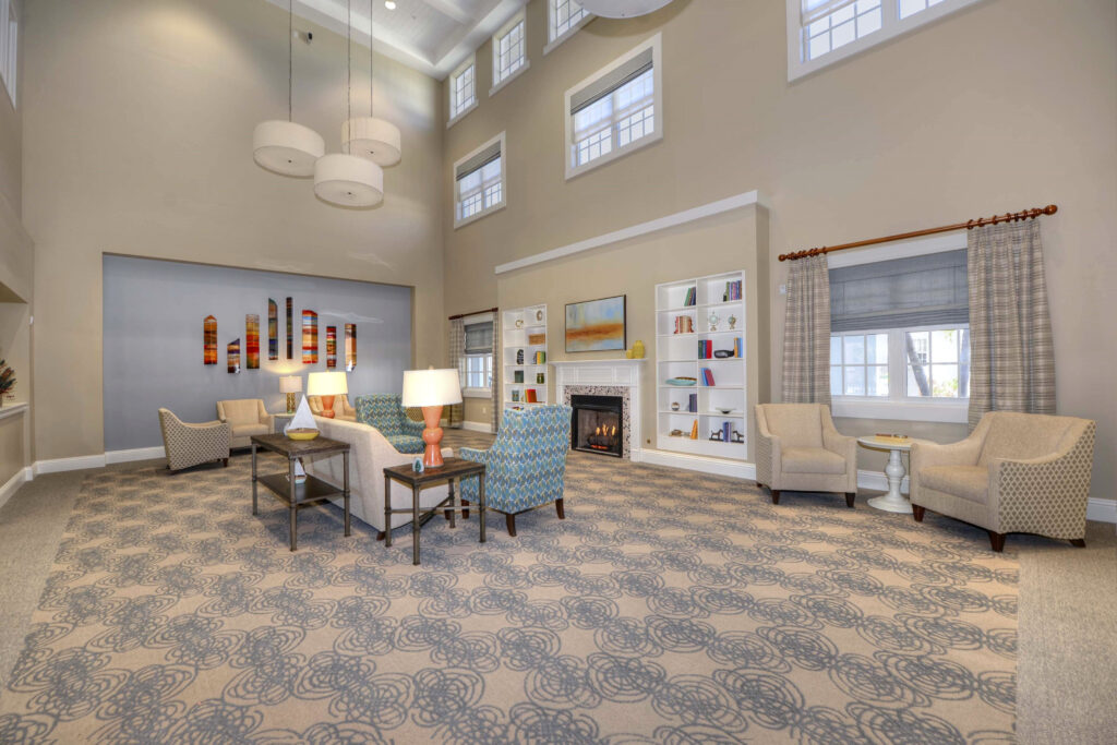 A sitting are with beige, blue, and green sofa chairs, fireplace, and white bookshelves that are built into the wall at Beach House, a senior living community.