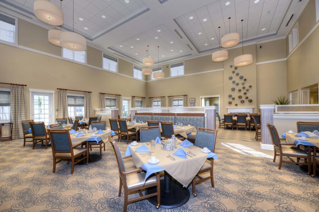 Beach House, a senior living community, main dining room with square tables, brown chairs, beige table cloths and blue napkins.