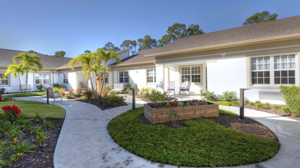 Beach House Memory Care courtyard with a walking path, garden, palm trees, and benches for sitting.