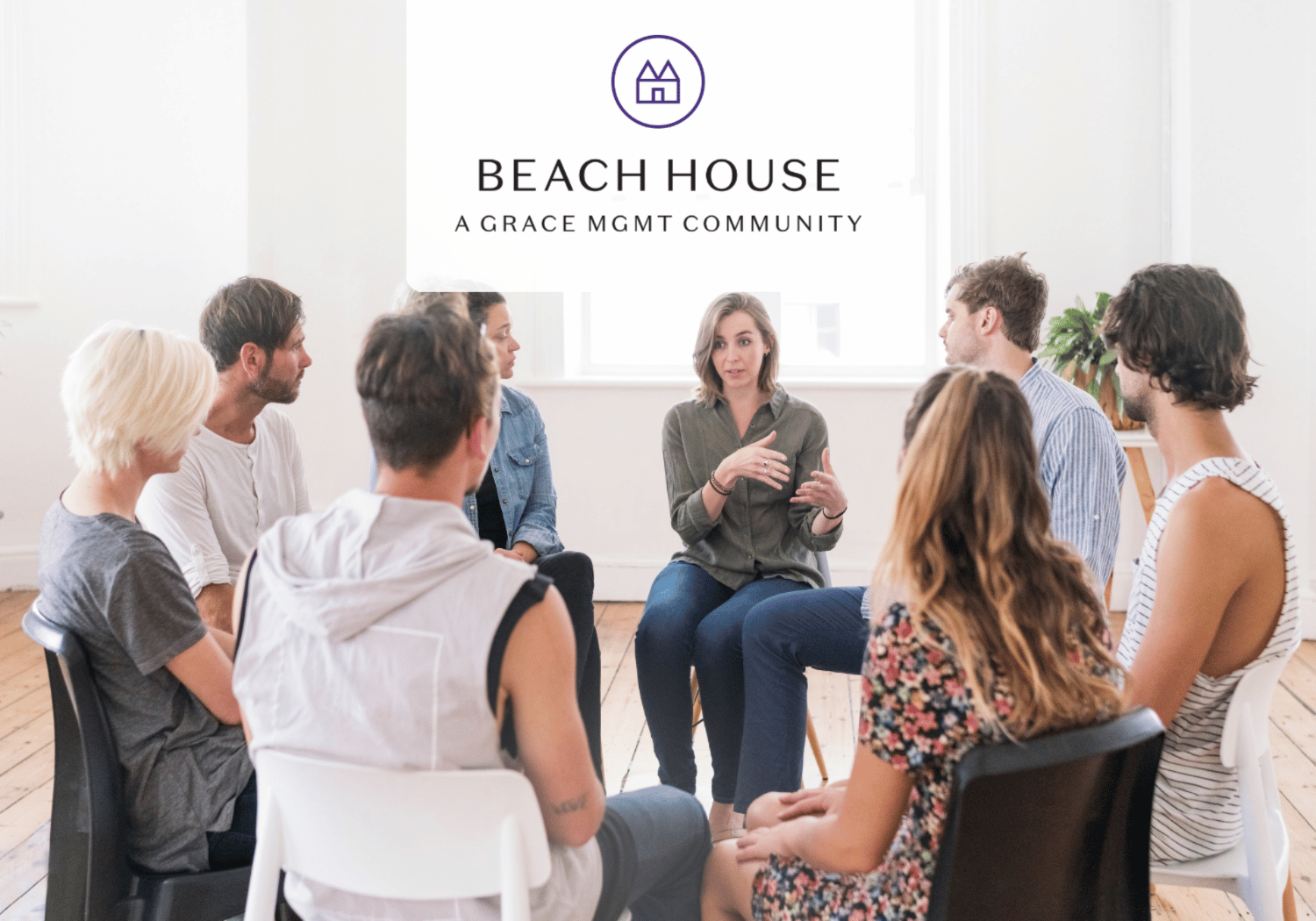 People seated in a circle in a bright room; a woman speaks as banner reads Beach House, A Grace Mgmt Community.